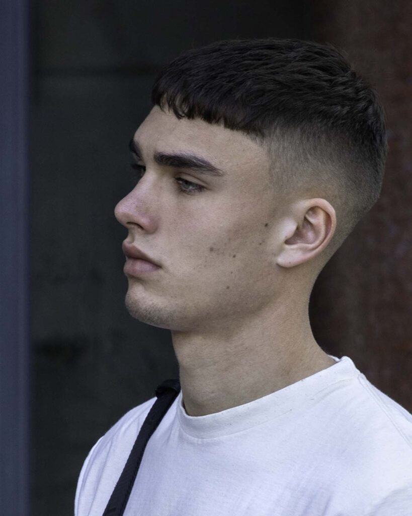 Young person with fade haircut, wearing white t-shirt and a bag over the shoulder