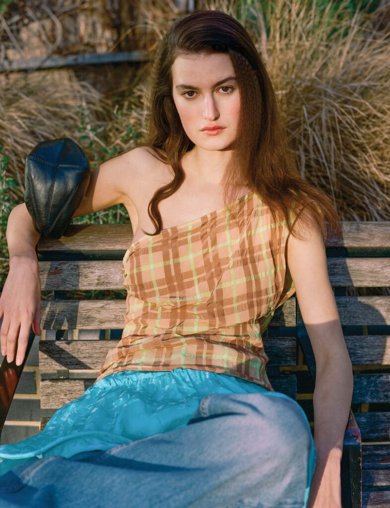 Model sits on a bench in check top and blue skirt