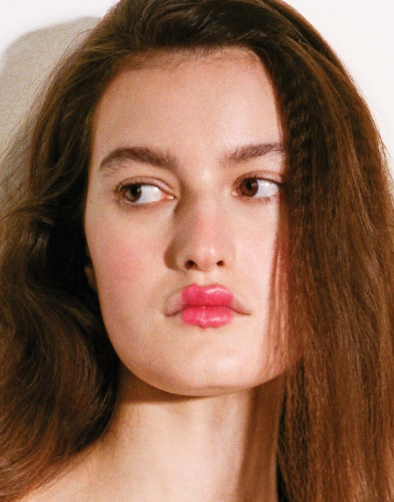 Close-up of model looking sideways with bright red lipstick applied to the centre of the lip only, for a pinched effect