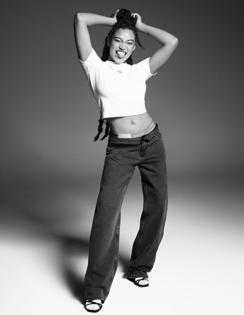 Full-length black and white image of Amandla Stenberg smiling in Calvin Klein