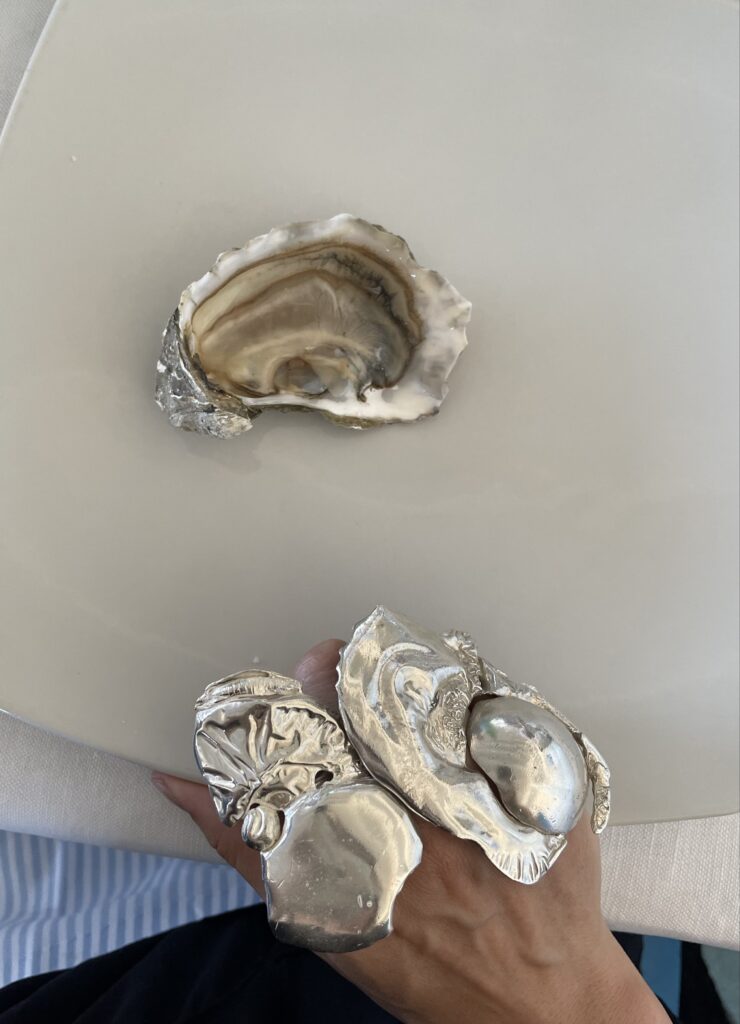 Photo of large, sea-shell inspired jewellery with a shell sitting behind on a table