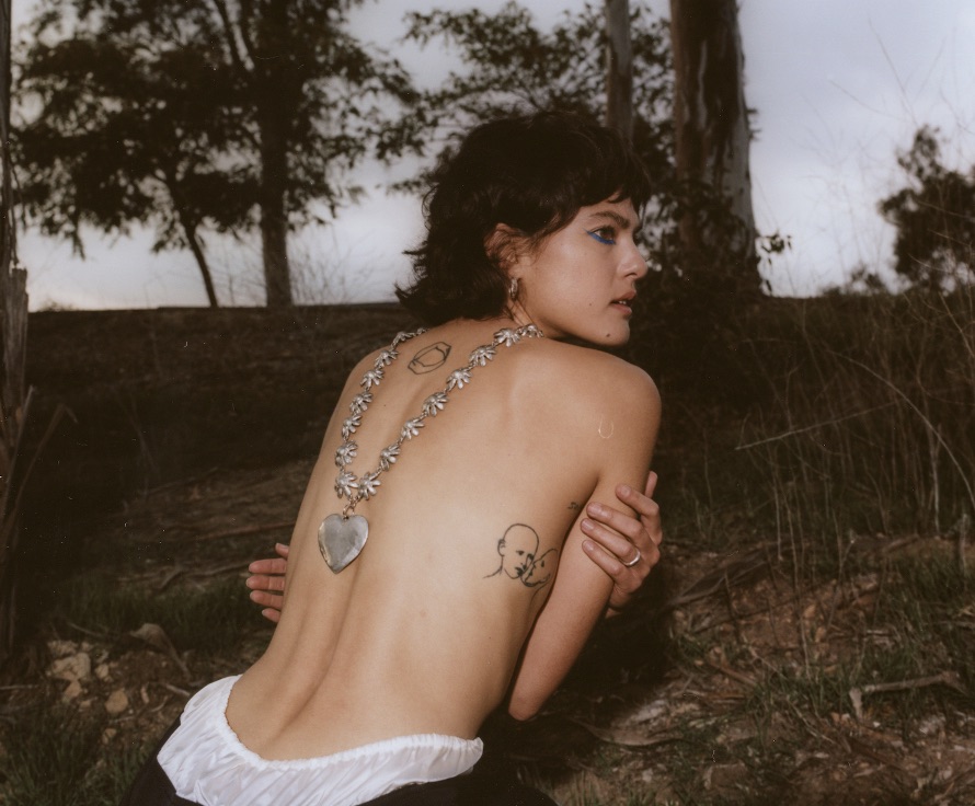 Analogue photograph of Miya Folick crouched half-naked outdoors, facing away from the camera