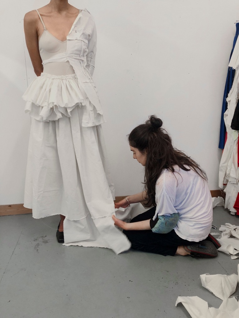 Camera roll image of a designer kneeling working on a dress while worn by a model
