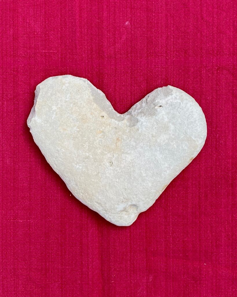 Close up image of a white heart-shaped stone against a pink background